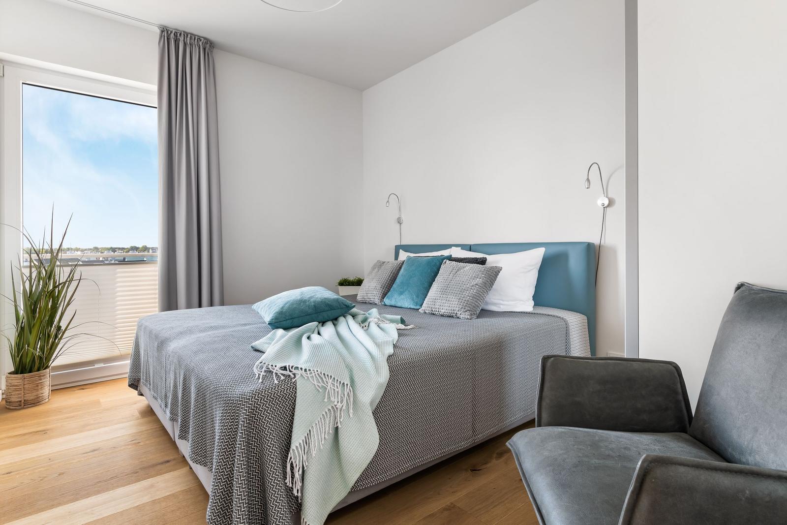 Bedroom with bed, armchair, and view of water through window.