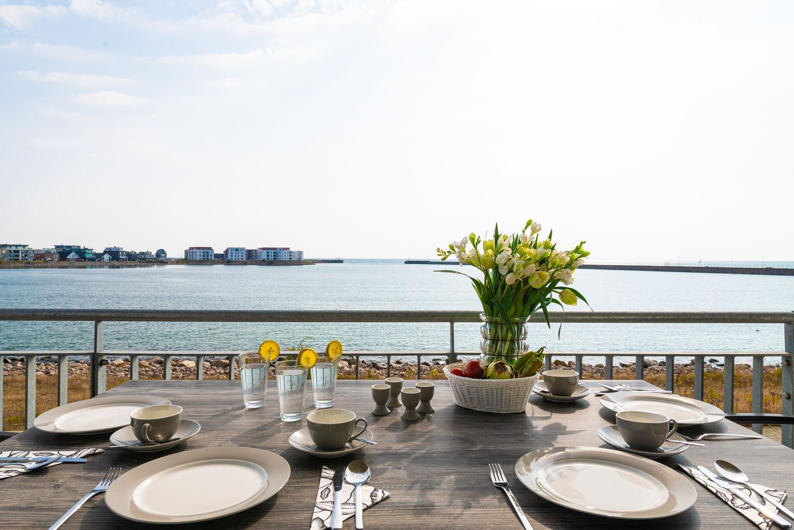 Gedeckter Tisch mit Meerblick, Blumen und Obst auf Balkon.