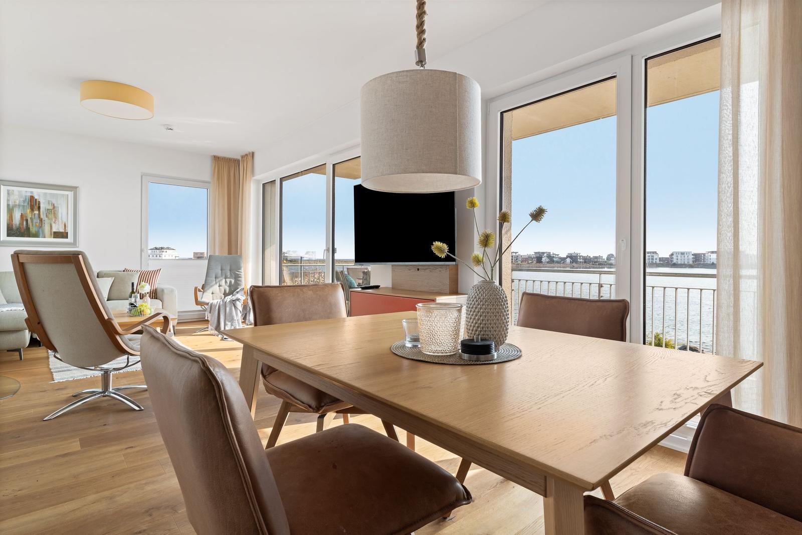 Essbereich mit Tisch und Stühlen, große Fenster mit Blick auf Wasser und Balkon.
