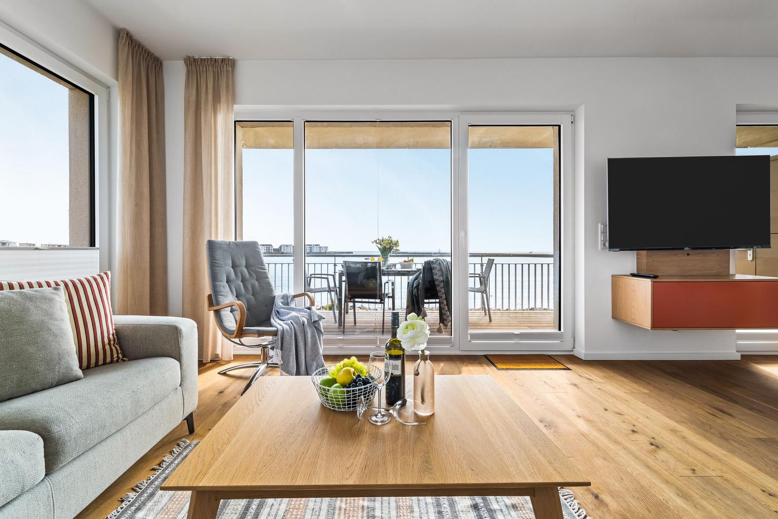 Wohnzimmer mit Balkonblick, Sofa, Fernseher und Holzboden.