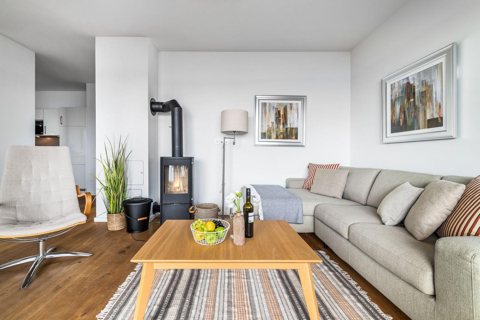 Wohnzimmer mit Sofa, Kamin und Holztisch. Küche im Hintergrund.