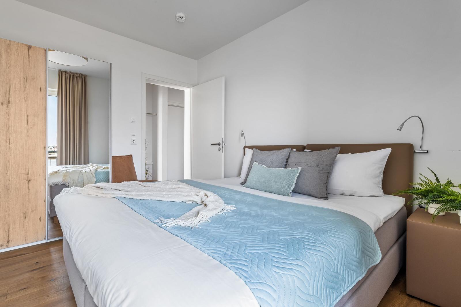 Schlafzimmer mit Bett, Nachttisch, Spiegel und Holzboden.