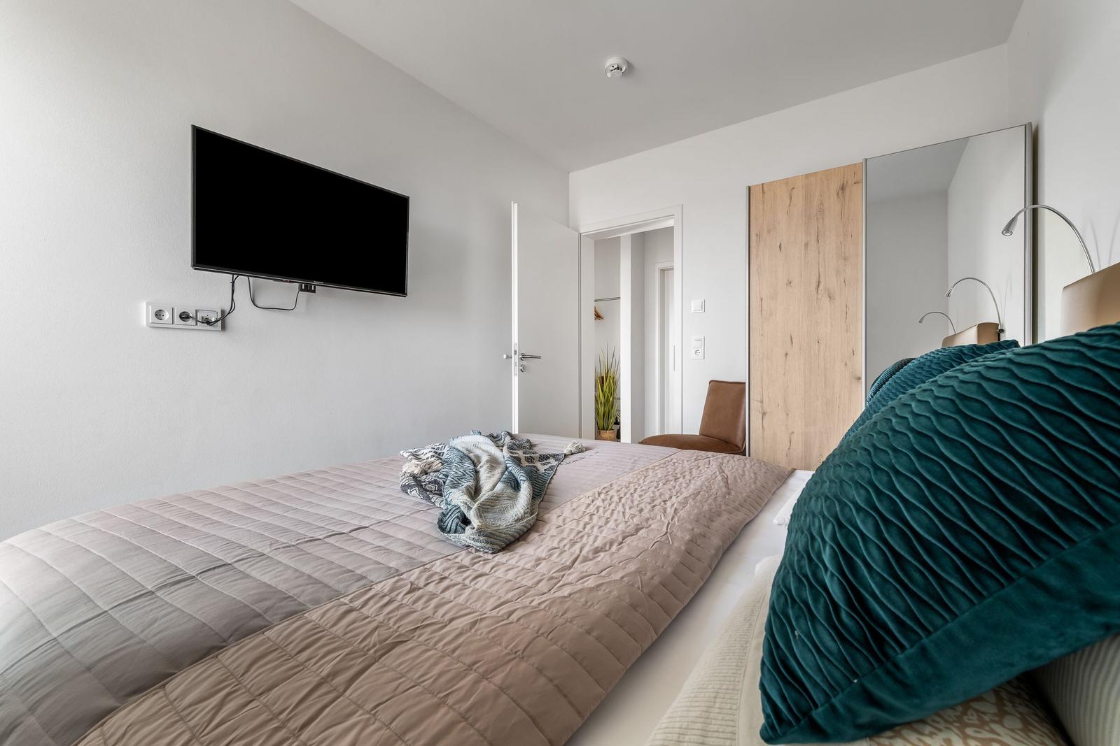 Schlafzimmer mit Bett, Fernseher und Spiegelschrank