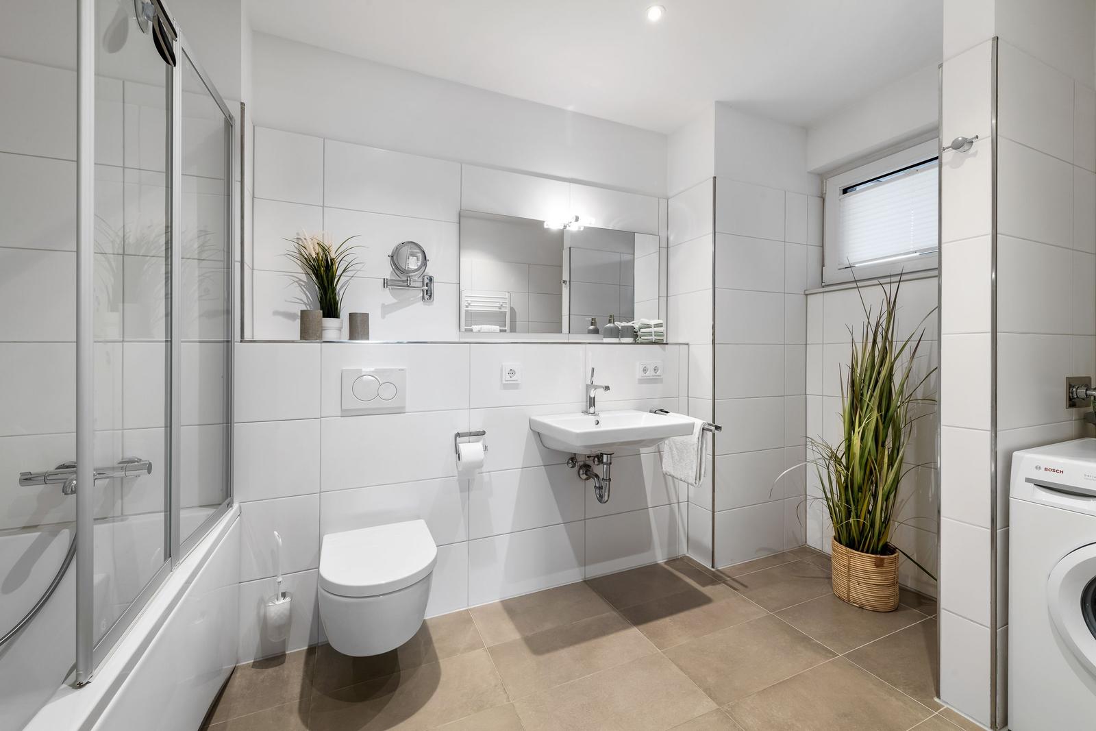 Badezimmer mit Dusche, Waschbecken, Toilette und Waschmaschine.