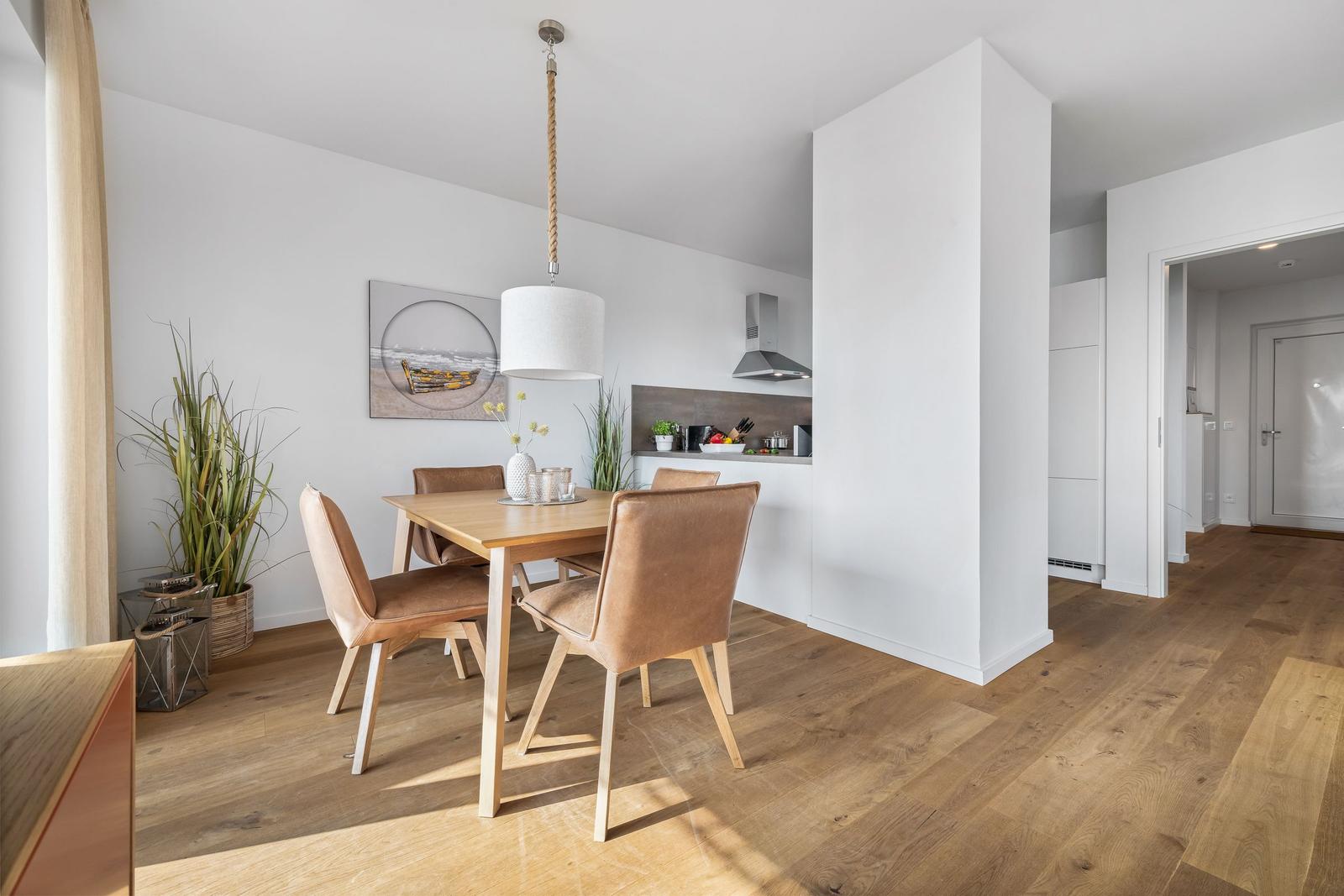 Essbereich mit Holztisch, braunen Stühlen und Küchenbereich im Hintergrund.