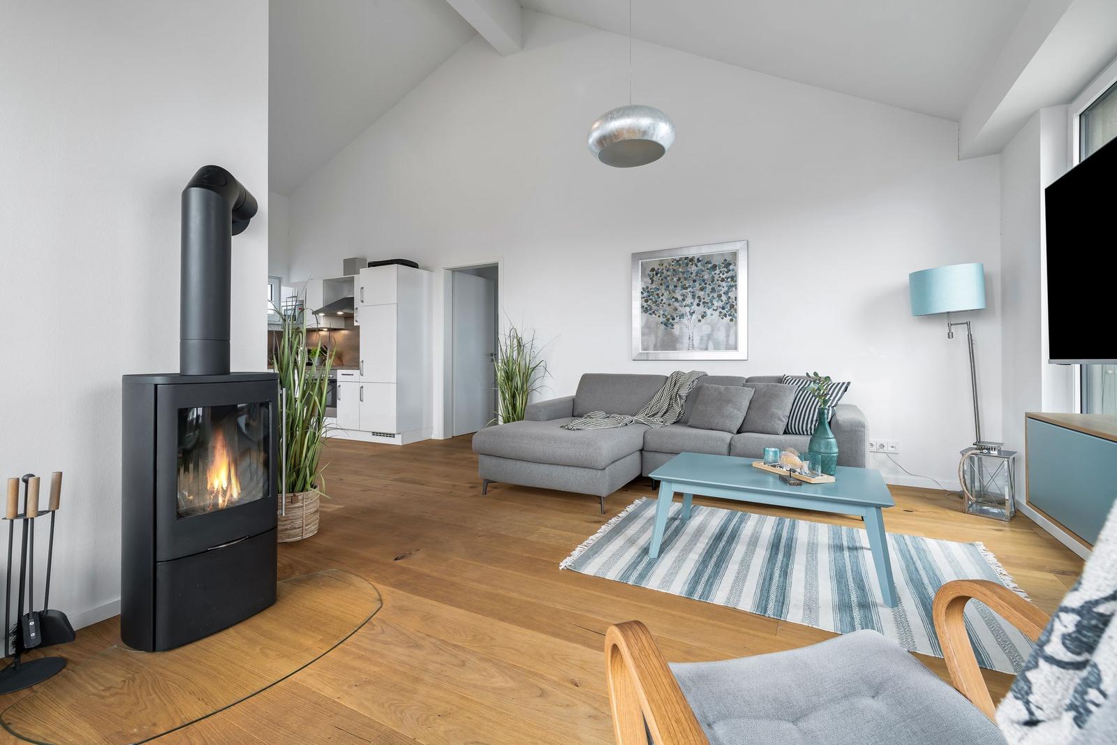 Wohnzimmer mit Kamin, Sofa und Holzboden. Küche im Hintergrund.