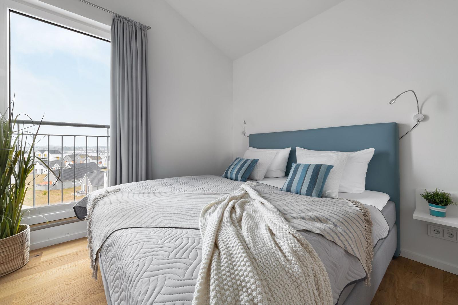 Schlafzimmer mit Bett, Fenster und Balkonblick.
