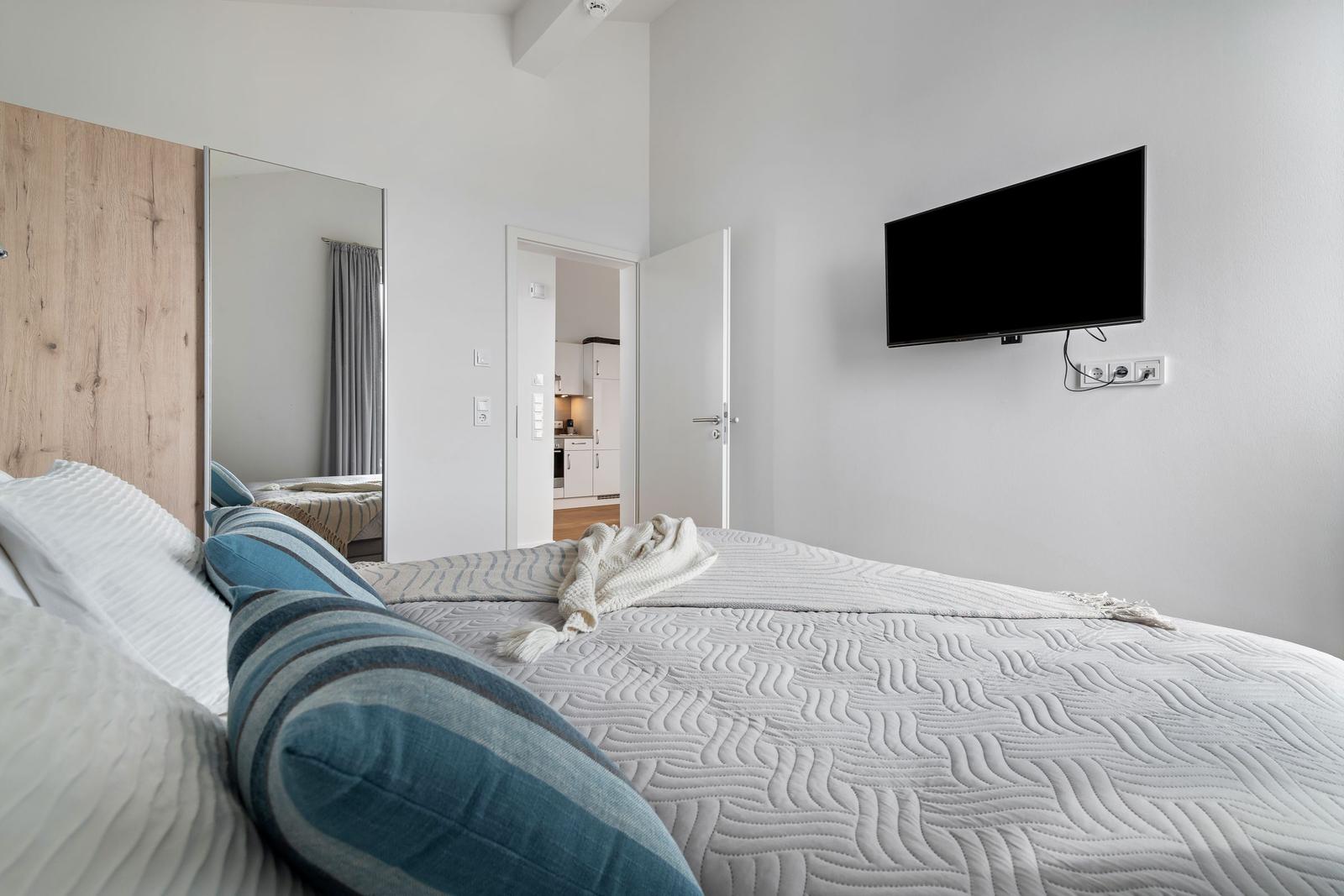 Schlafzimmer mit Bett, Fernseher und Blick in die Küche.