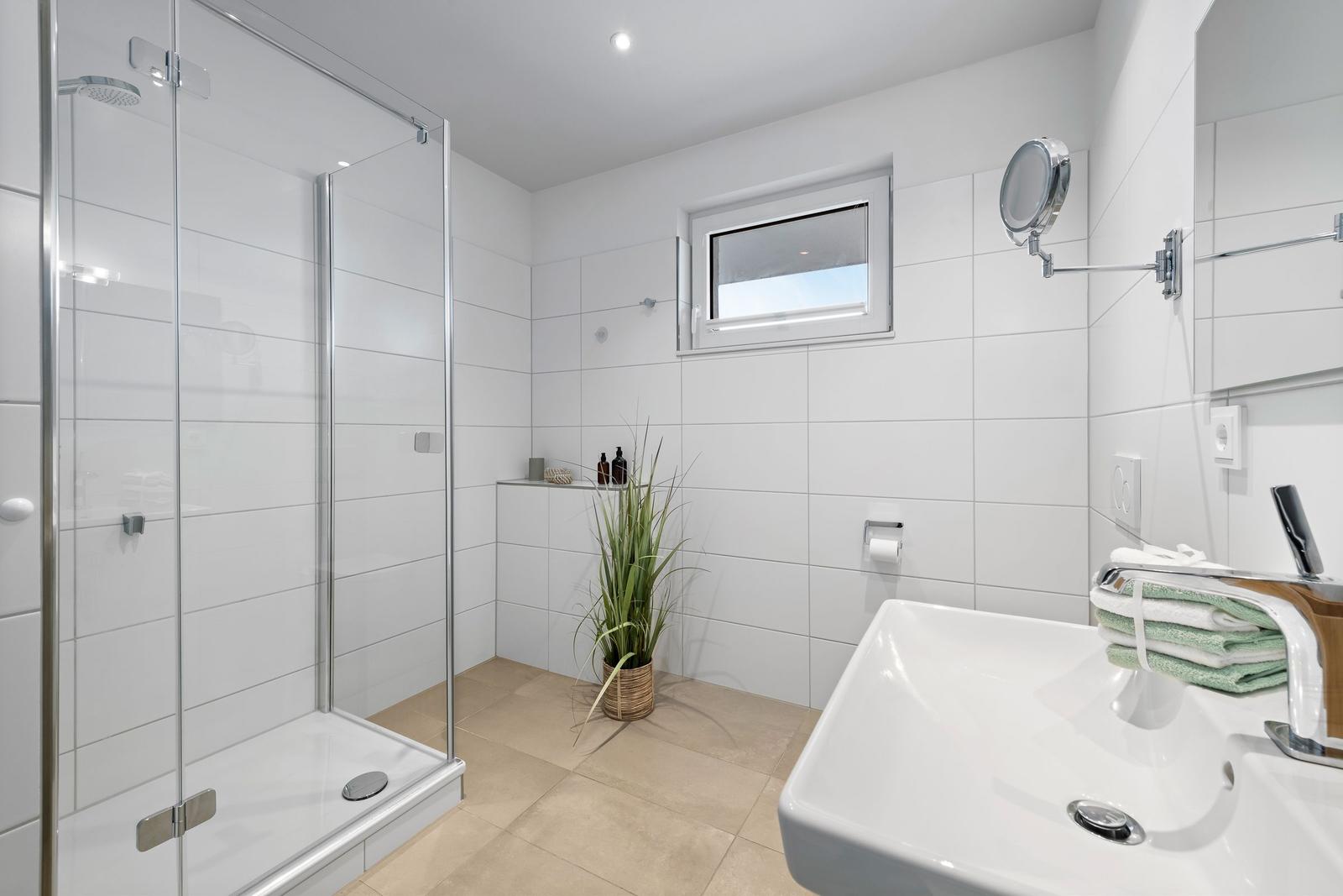 Badezimmer mit Dusche, Waschbecken und Pflanze.