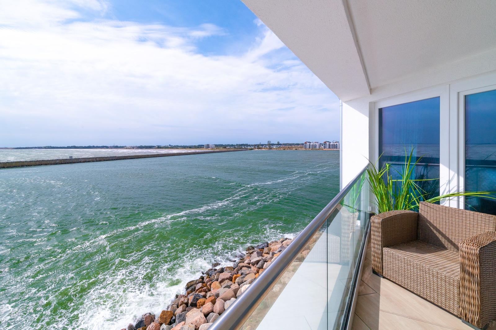 Terrasse mit Meerblick, Glasgeländer und Rattanmöbel. Blick auf Wasser und Steilküste.