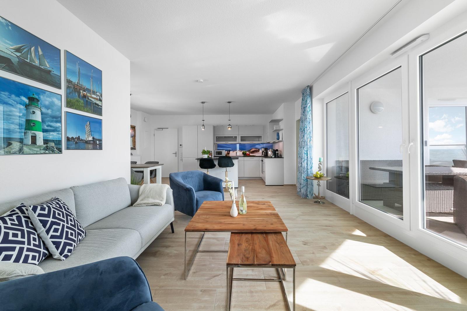 Wohnbereich mit Sofa, Couchtisch und Küchenbereich. Große Fenster mit Meerblick.