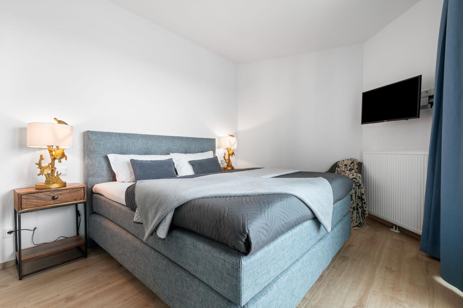 Schlafzimmer mit Bett, Nachttisch und Fernseher an der Wand.