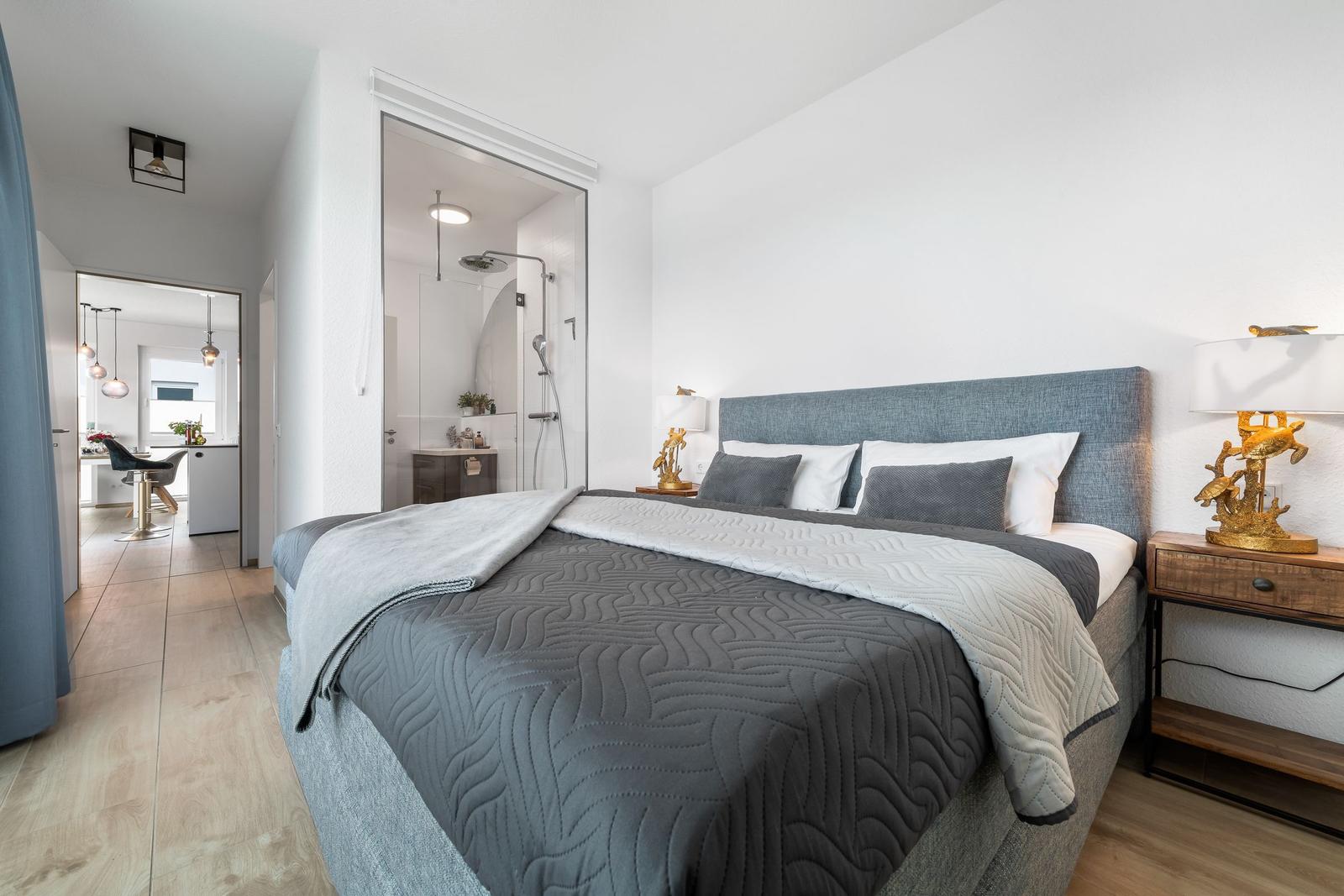 Schlafzimmer mit Doppelbett, Nachttisch und Blick in Bad und Küche.