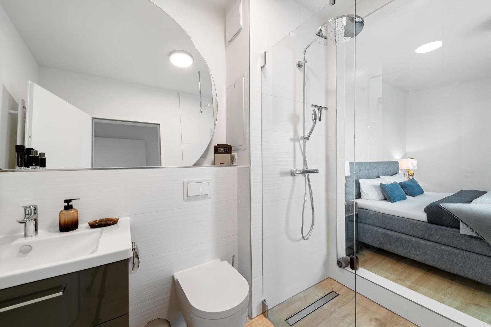 Badezimmer mit Dusche, Waschbecken und Toilette. Spiegel und moderne Einrichtung.