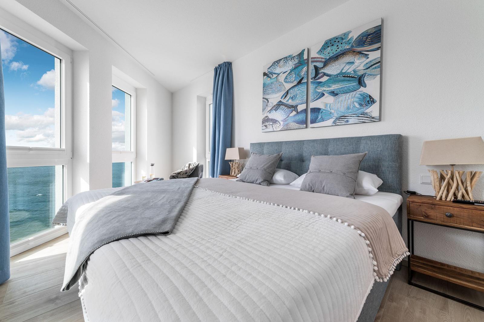 Schlafzimmer mit Blick aufs Meer, blauem Vorhang und Fischbildern an der Wand.