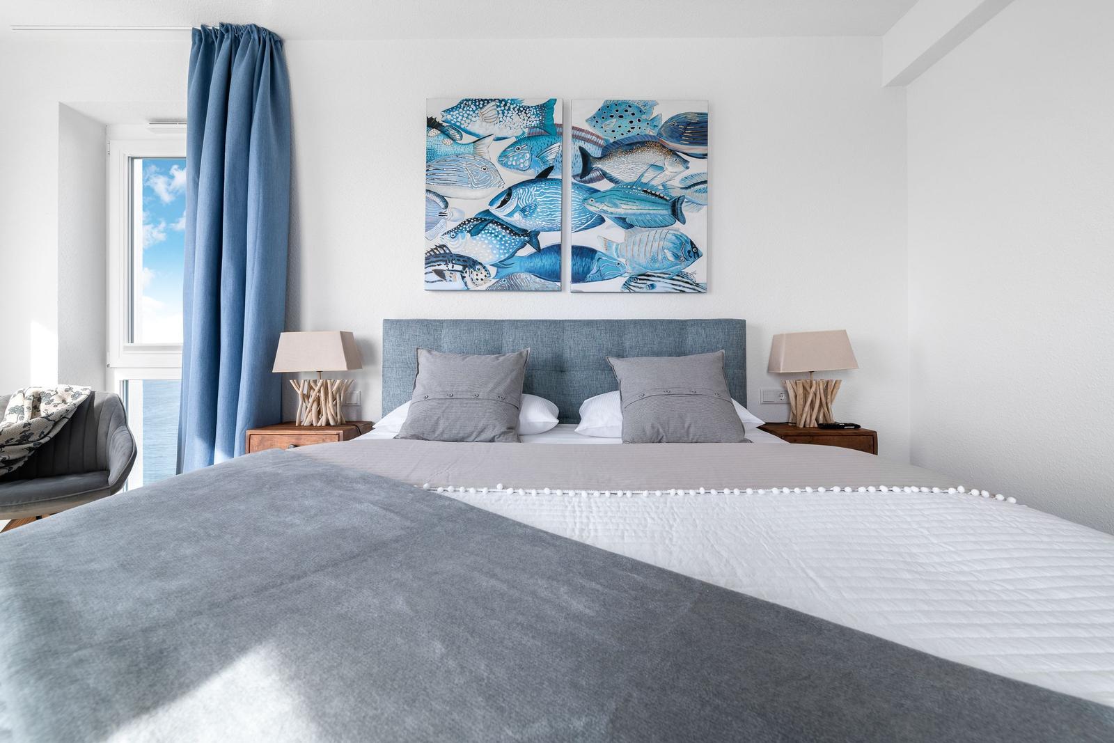 Schlafzimmer mit Bett, Fenster und Wandbildern mit Fischen.