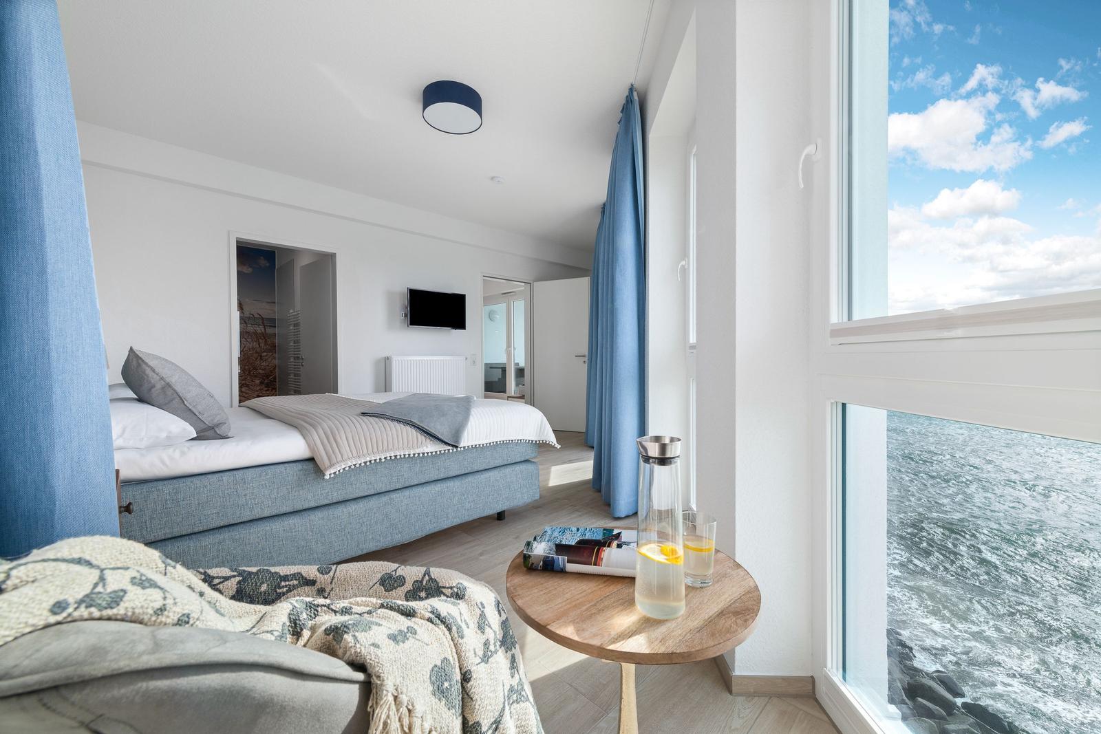Schlafzimmer mit Blick aufs Meer. Bett, Tisch und Fenster sind sichtbar.