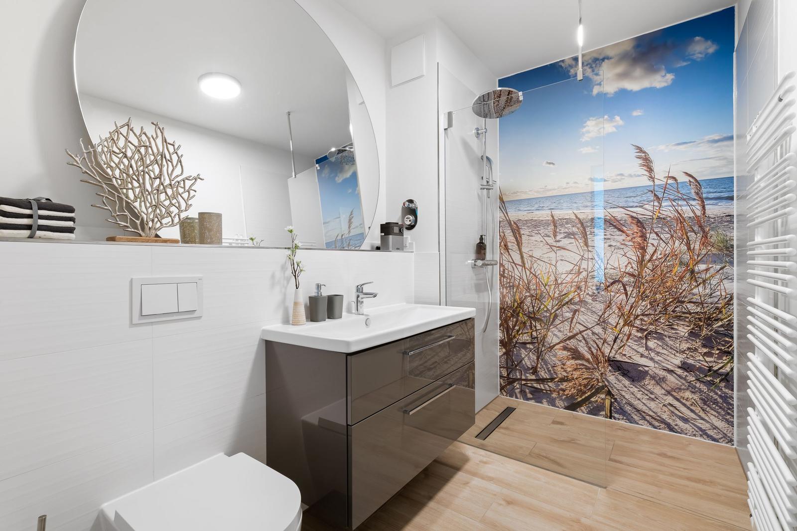 Badezimmer mit Dusche, Waschbecken und Spiegel. Wandbild zeigt Strand.