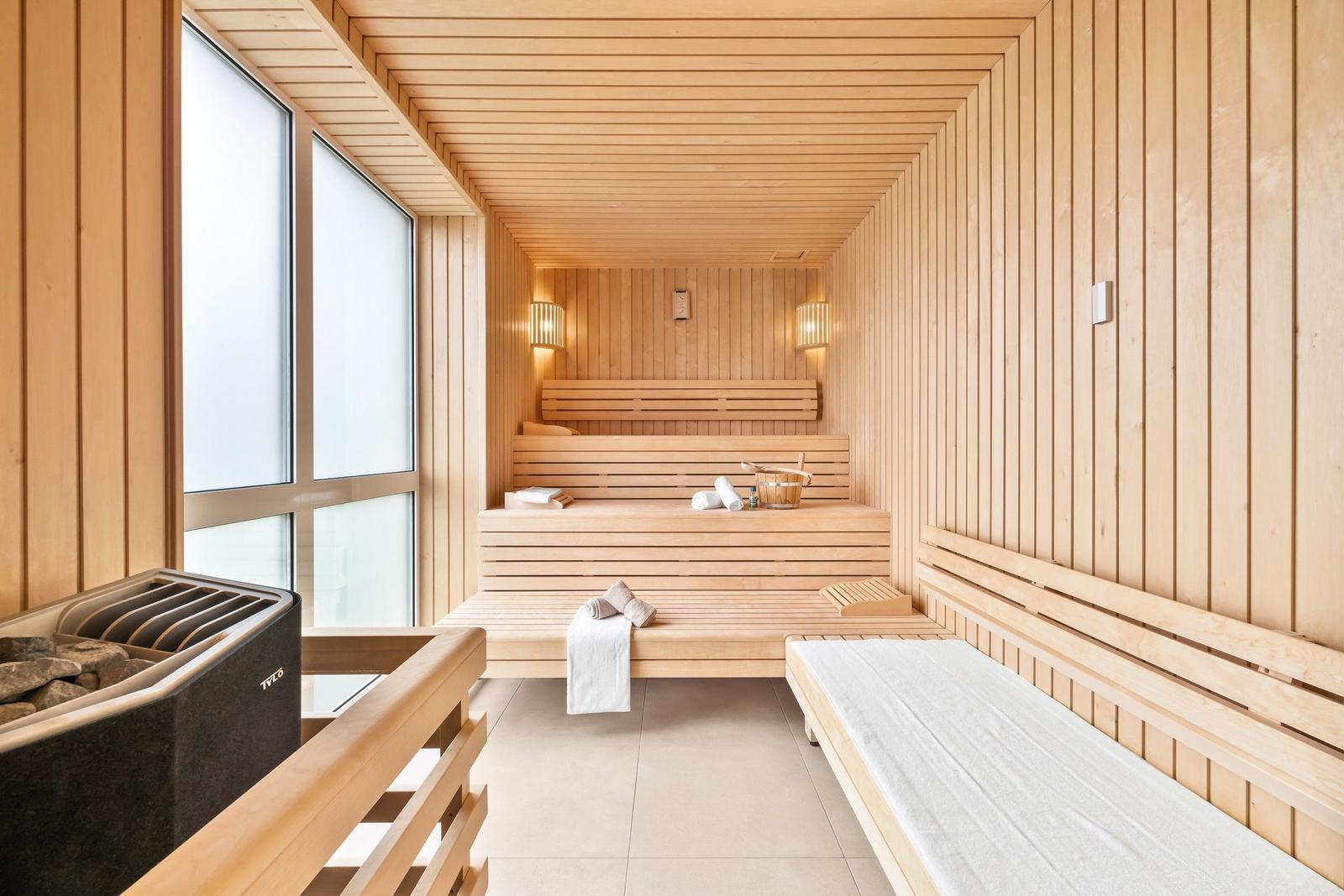Sauna mit Holzbanken, Fenster und Heizung. Handtücher und Eimer sind vorhanden.