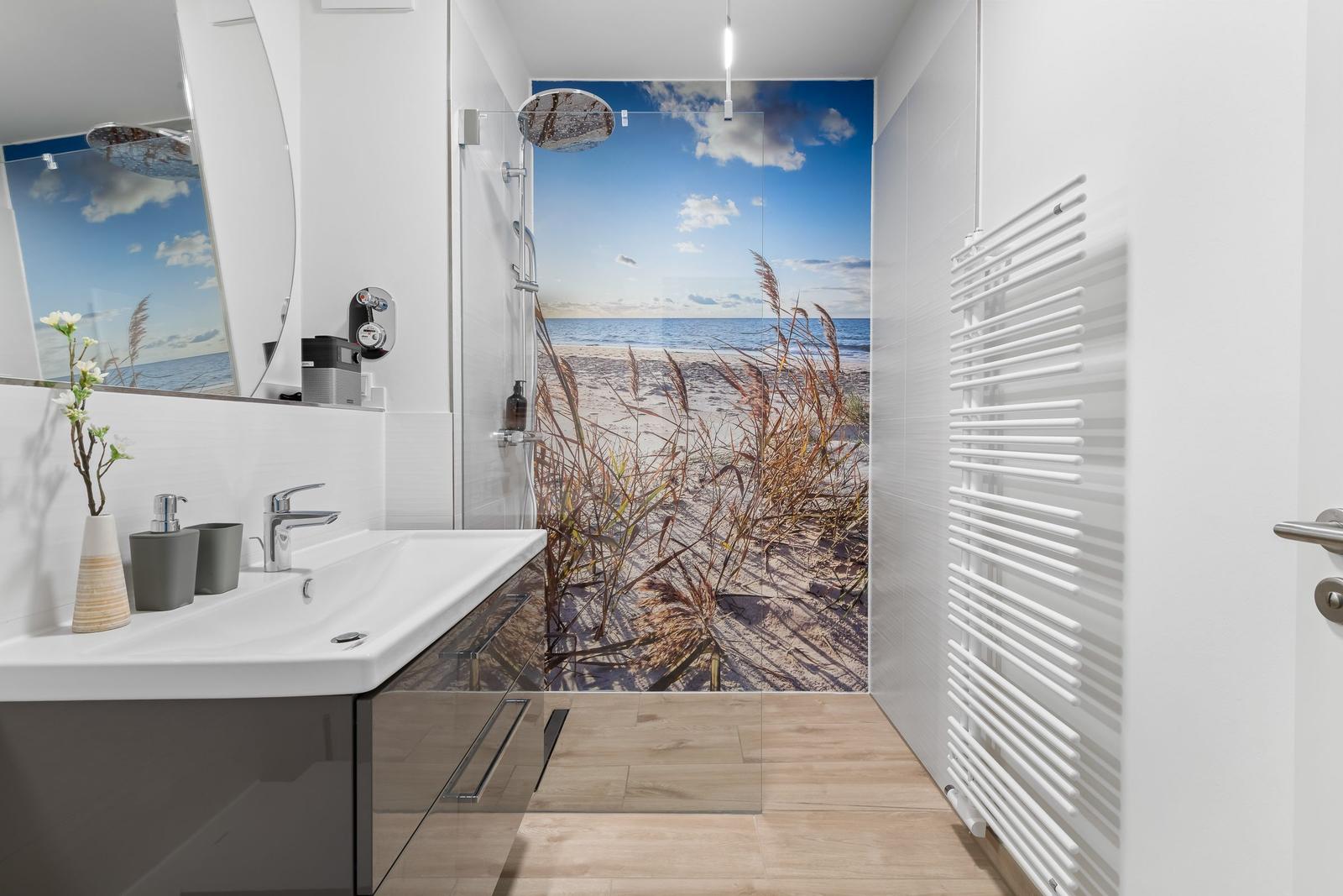 Badezimmer mit Dusche und Seeblicktapete. Waschbecken, Spiegel und Heizkörper sichtbar.
