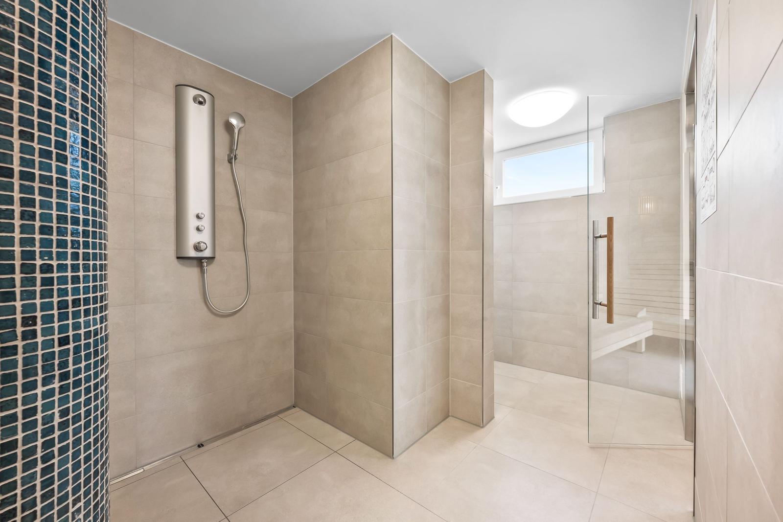 Dusche mit Duschbrause und Glaswand. Sauna mit Sitzbank und Fenster.