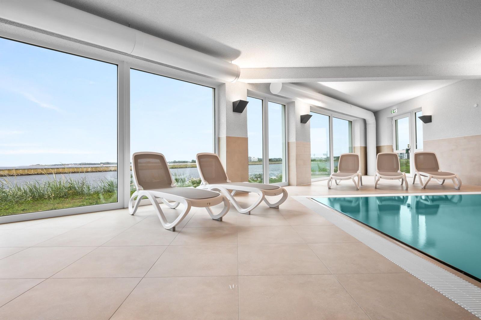 Indoorpool mit Liegestühlen und Blick auf Wasser