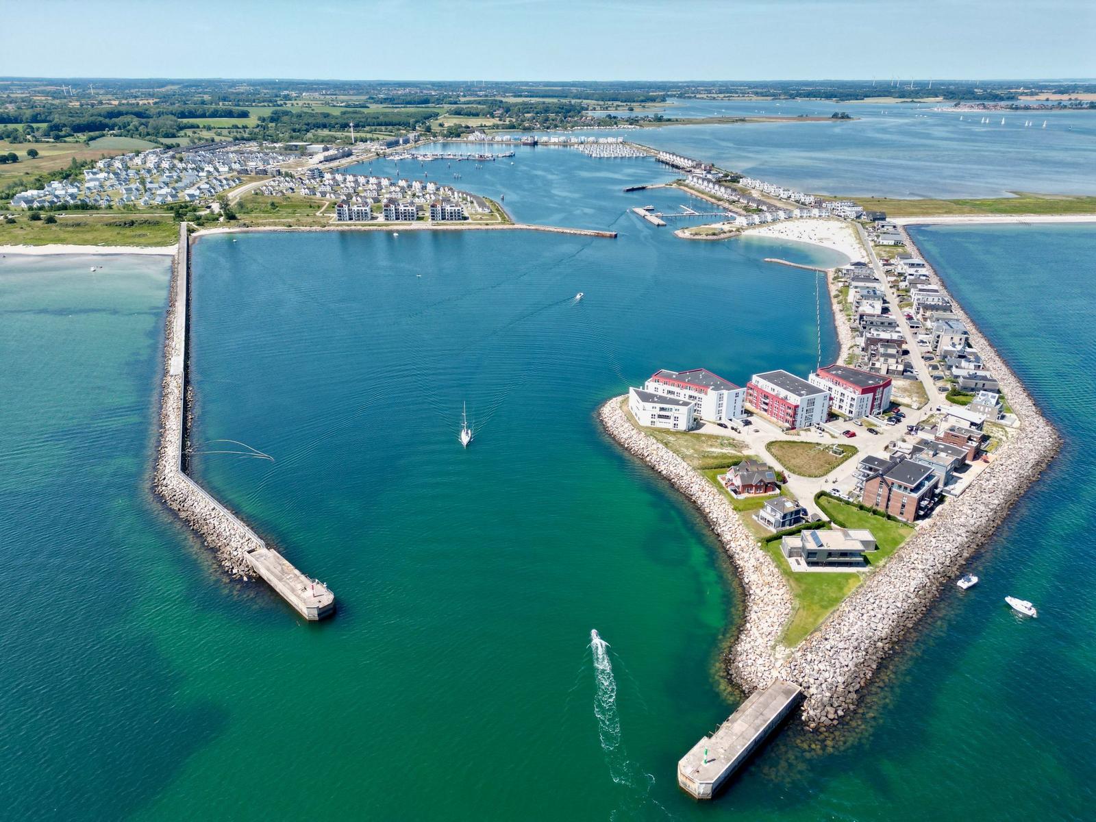 Aerial view of a harbor with boats, waterfront buildings, and surrounding green areas.