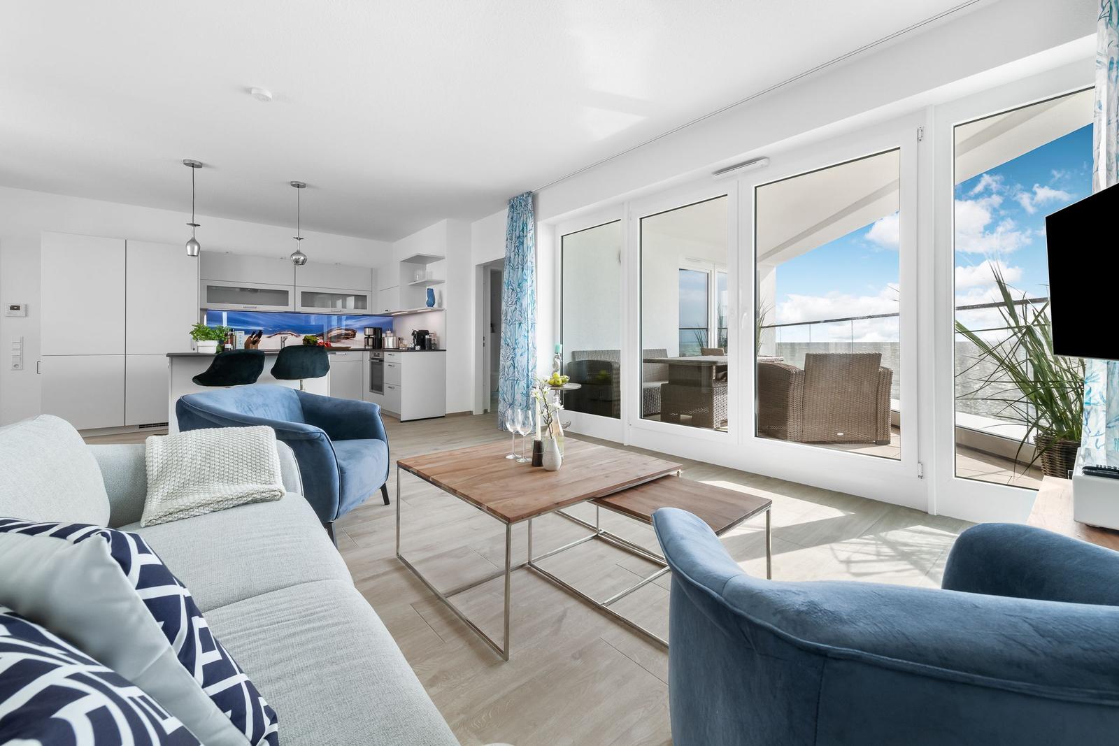 Wohnbereich mit Küche und Balkon. Moderne Einrichtung mit blauen Sesseln und Holztisch.