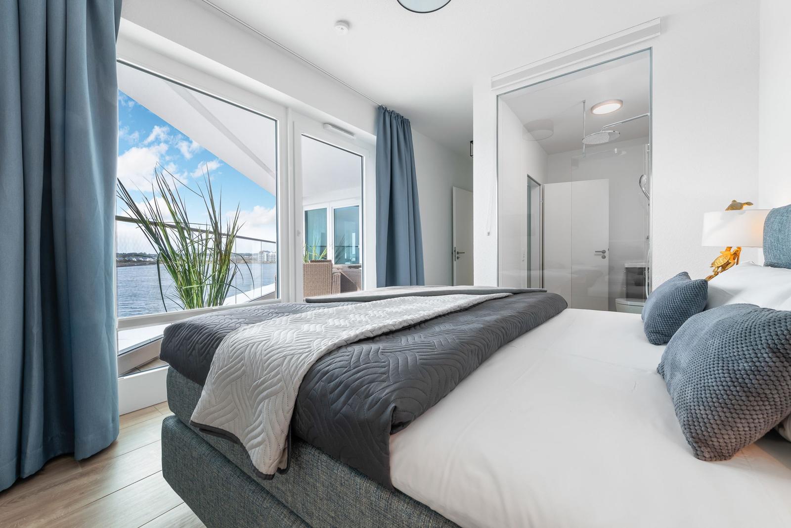 Schlafzimmer mit Blick auf Wasser, großes Bett und angrenzende Dusche.