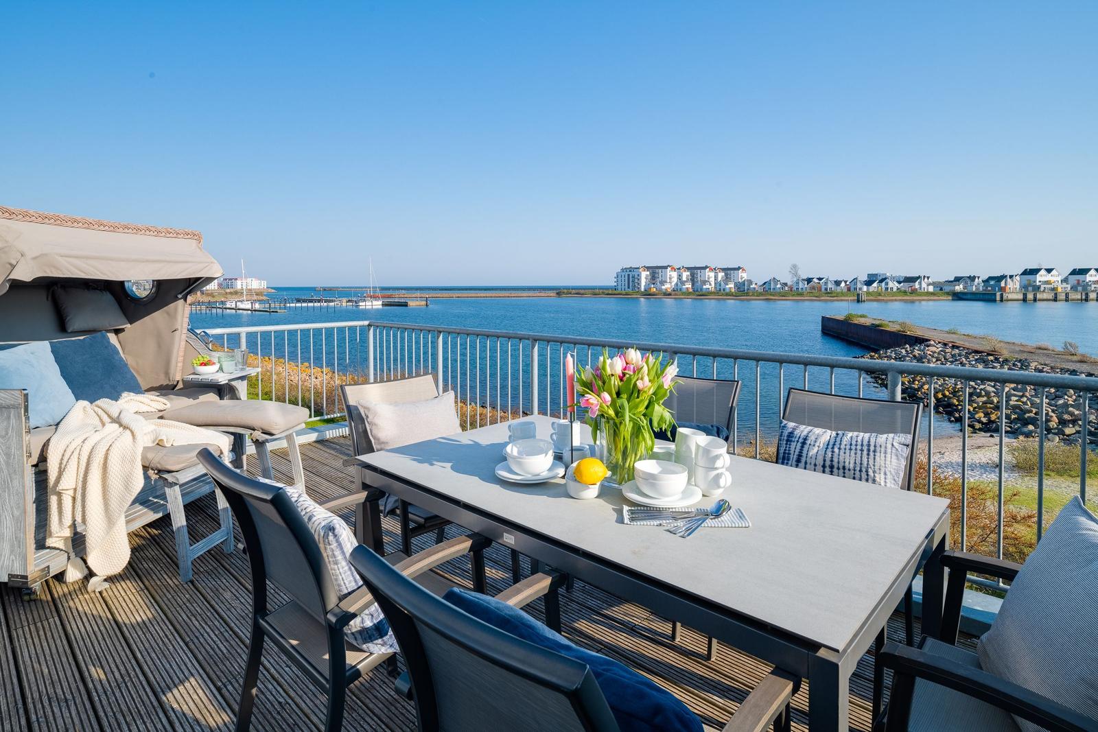 Terrasse mit Tisch, Stühlen und Blick auf Wasser und Ufer.