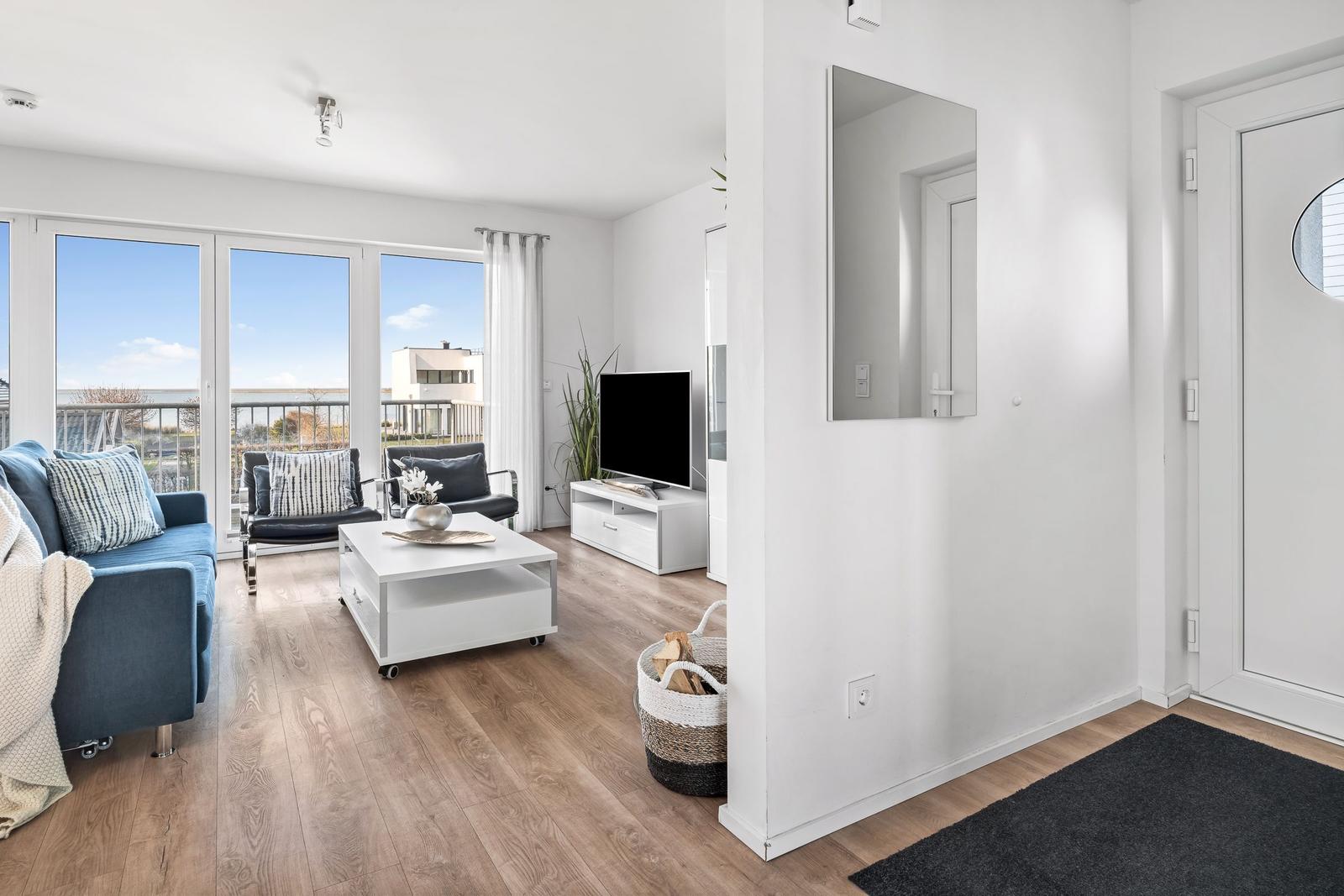 Wohnzimmer mit Sofa, Couchtisch und TV. Terrasse mit Blick auf den Himmel.