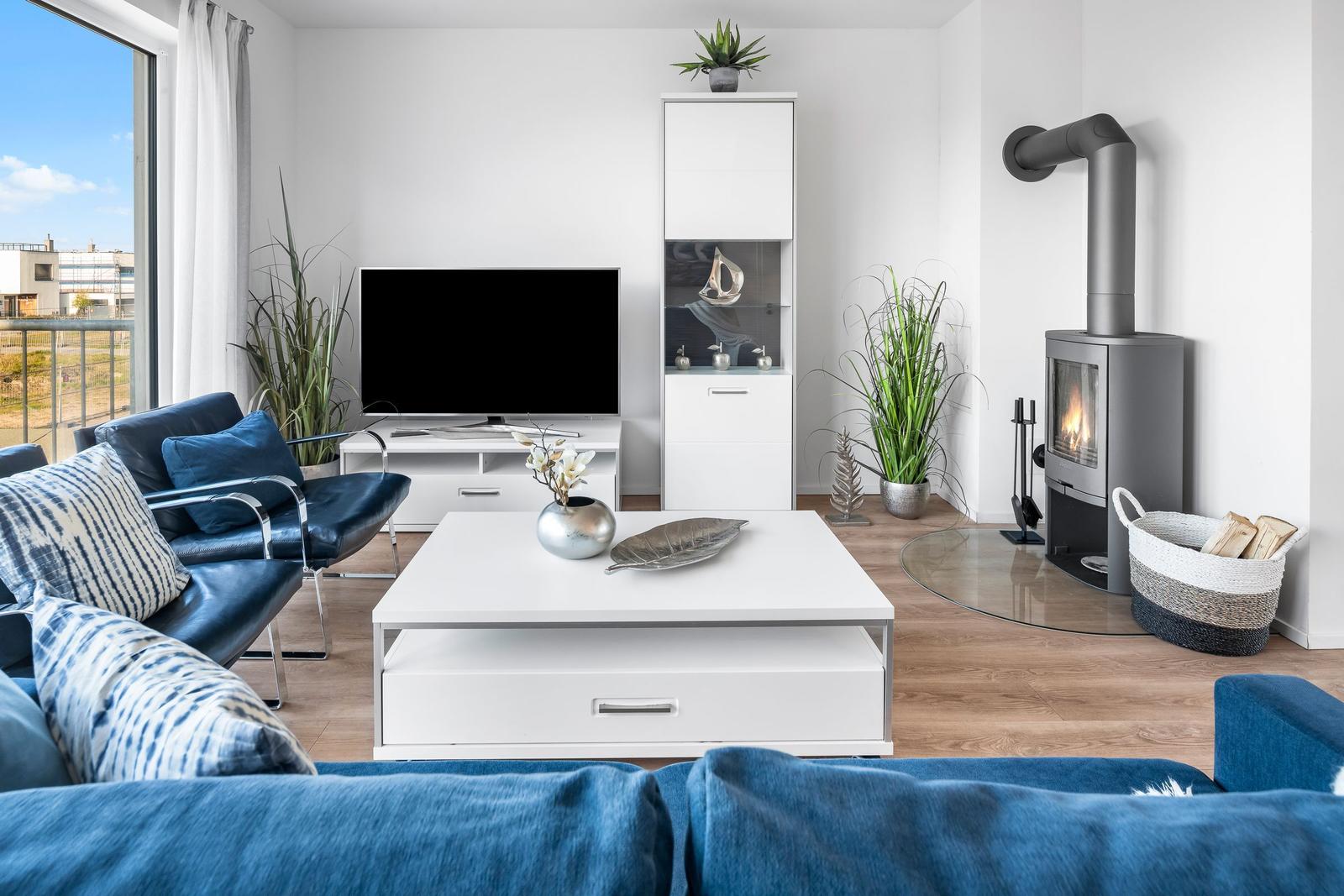 Wohnzimmer mit Sofa, Fernseher, Kamin und großen Fenstern.