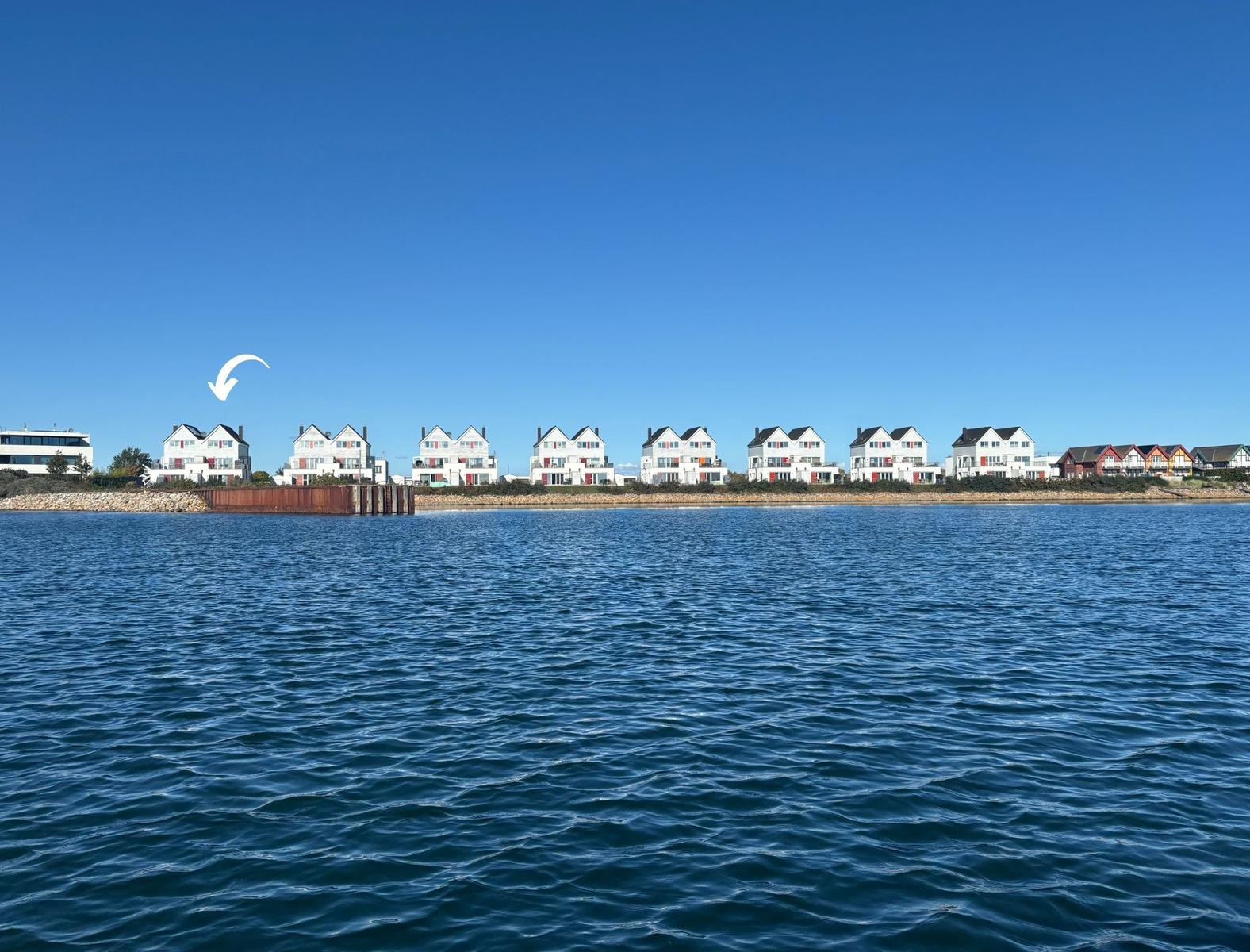 Wohnhäuser am Wasser mit klarem Himmel und ruhiger Seeoberfläche.