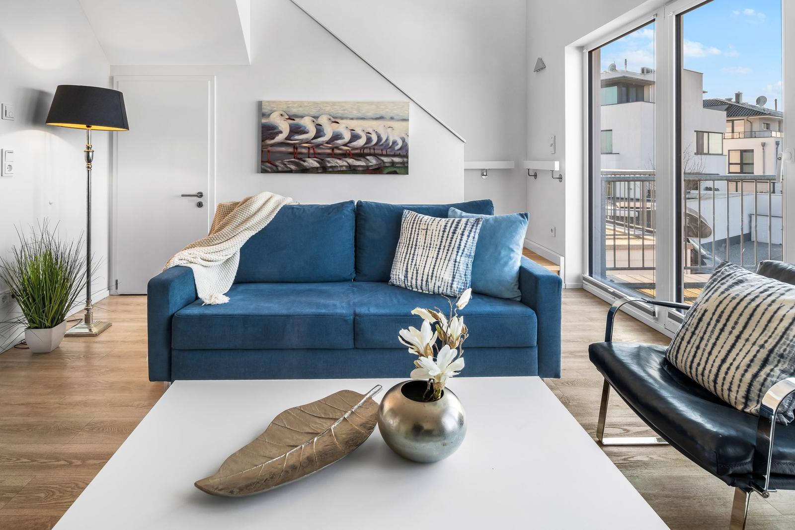 Blauer Sofa mit Kissen und Decke im Wohnzimmer mit Blick auf Balkon.