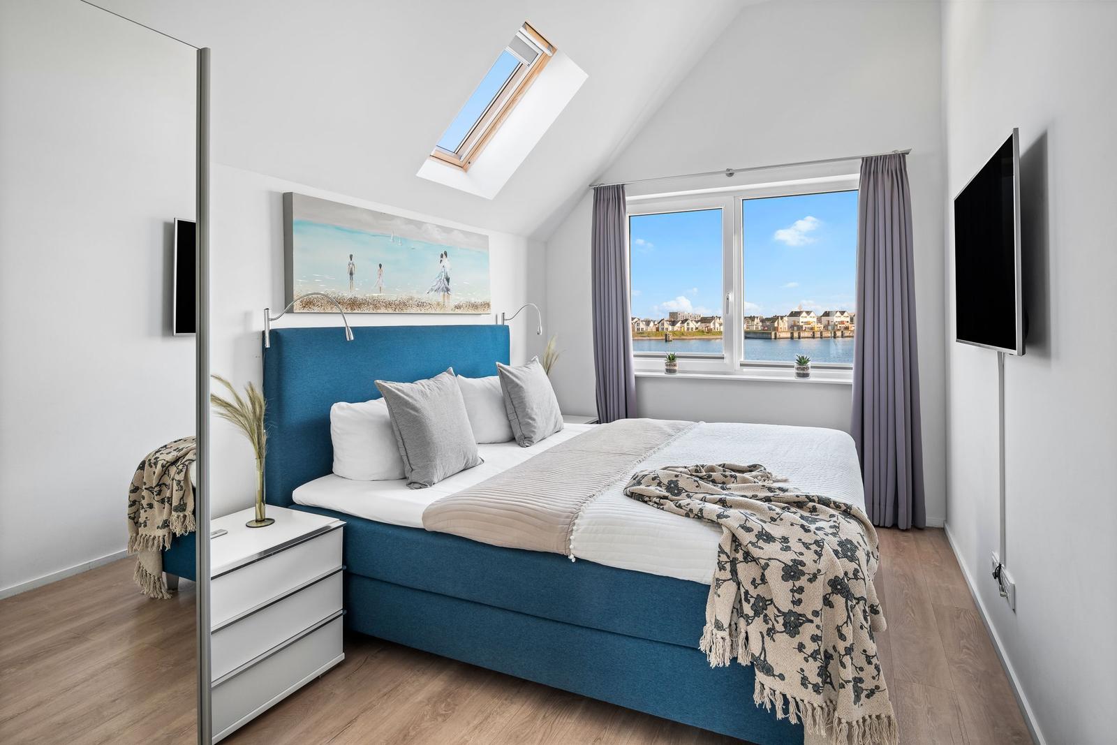 Schlafzimmer mit Dachfenster, Bett und Fenster mit Blick auf Wasser.
