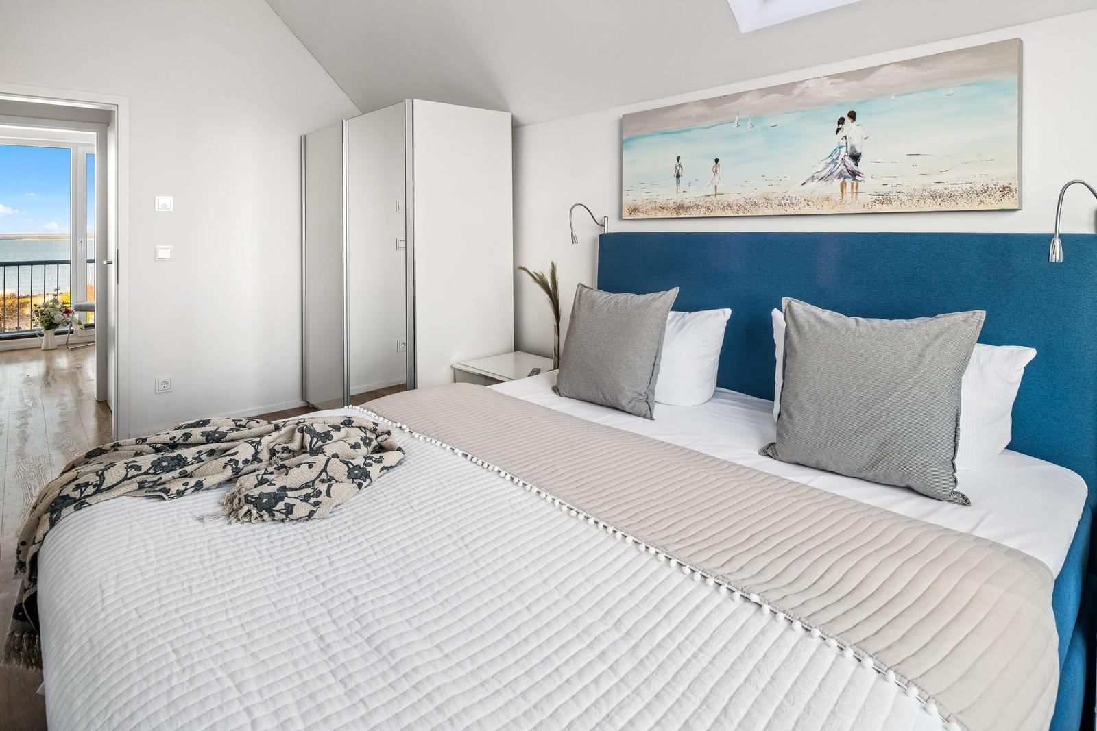Schlafzimmer mit Bett, blauem Kopfteil und Blick auf Balkon.