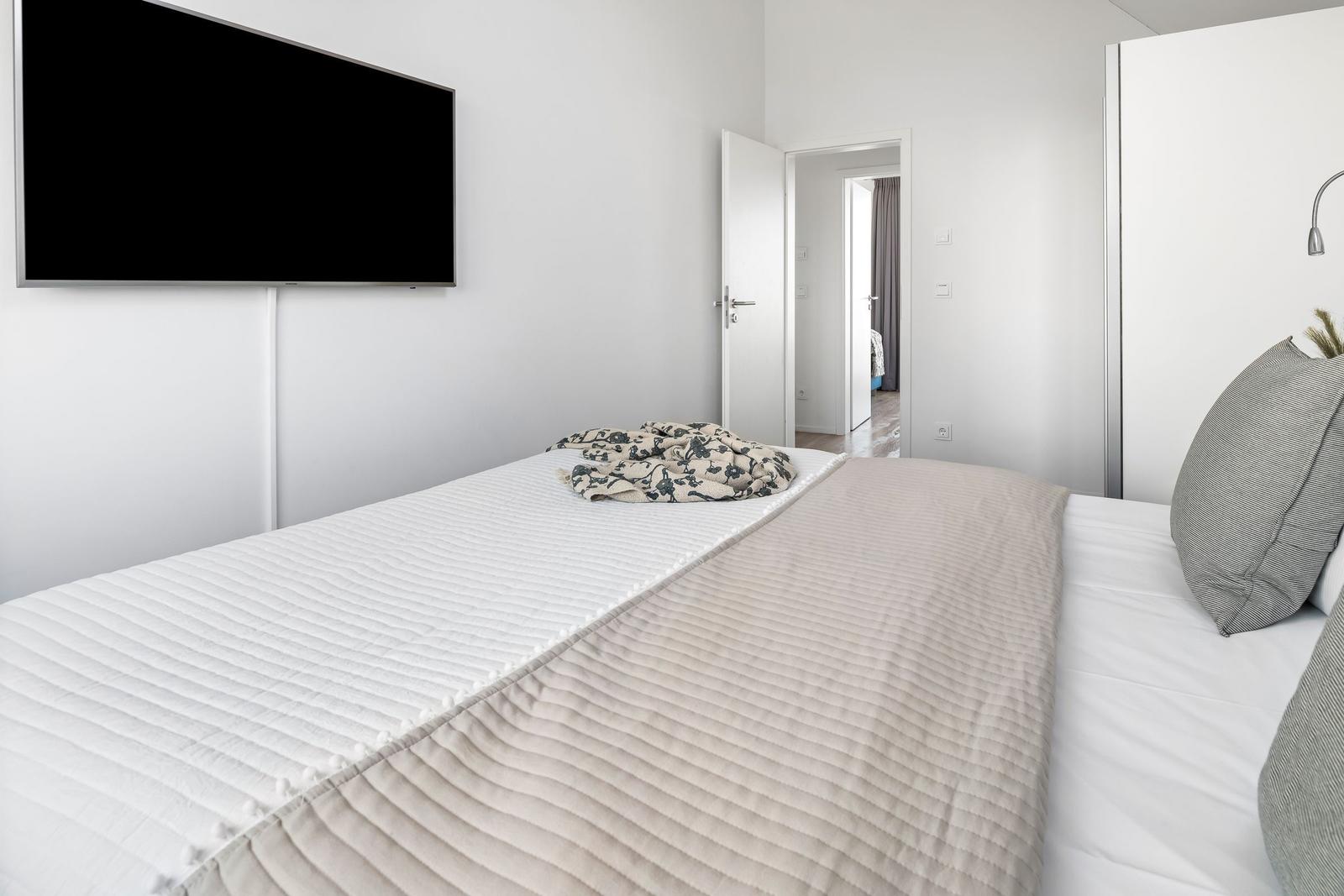 Schlafzimmer mit Bett, Fernseher und Blick in einen angrenzenden Raum.