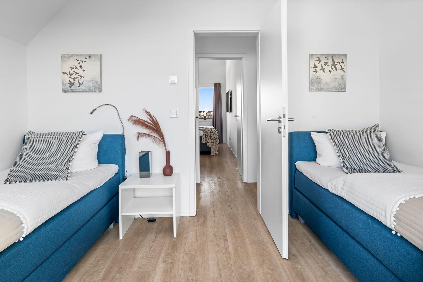 Zwei Schlafzimmer mit blauen Betten und Holzboden. Durchgang zu weiterem Raum.
