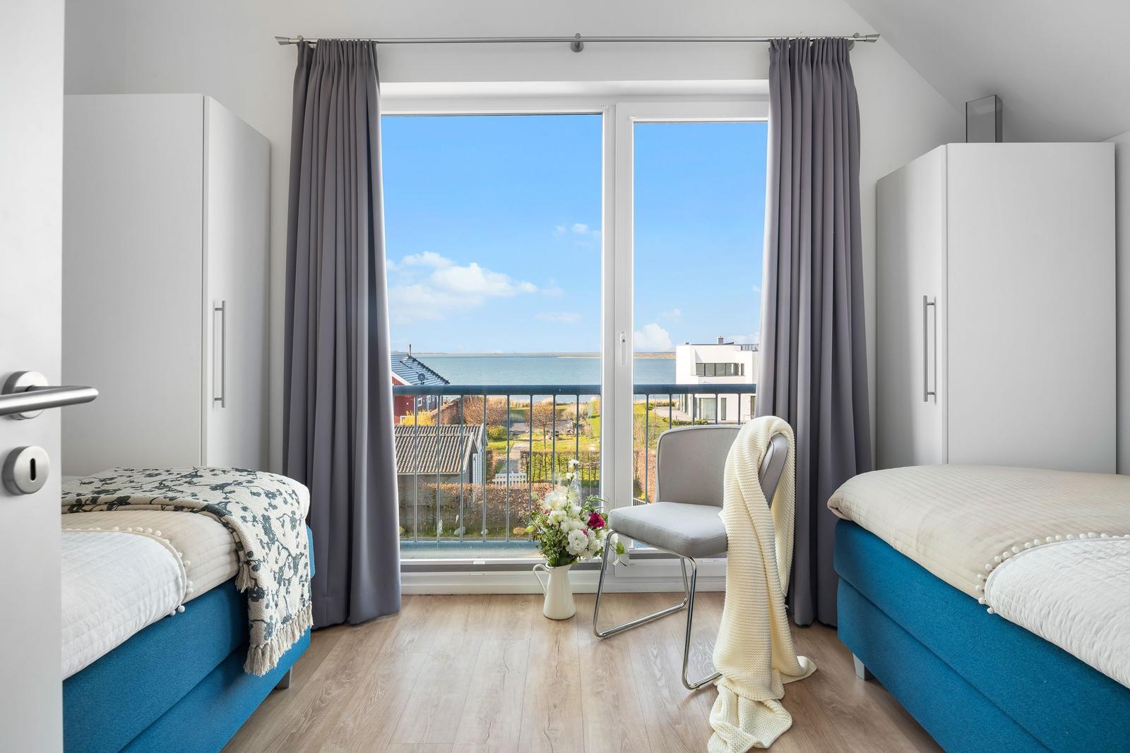 Zwei Betten mit Blick aufs Meer und Balkon mit Stuhl.