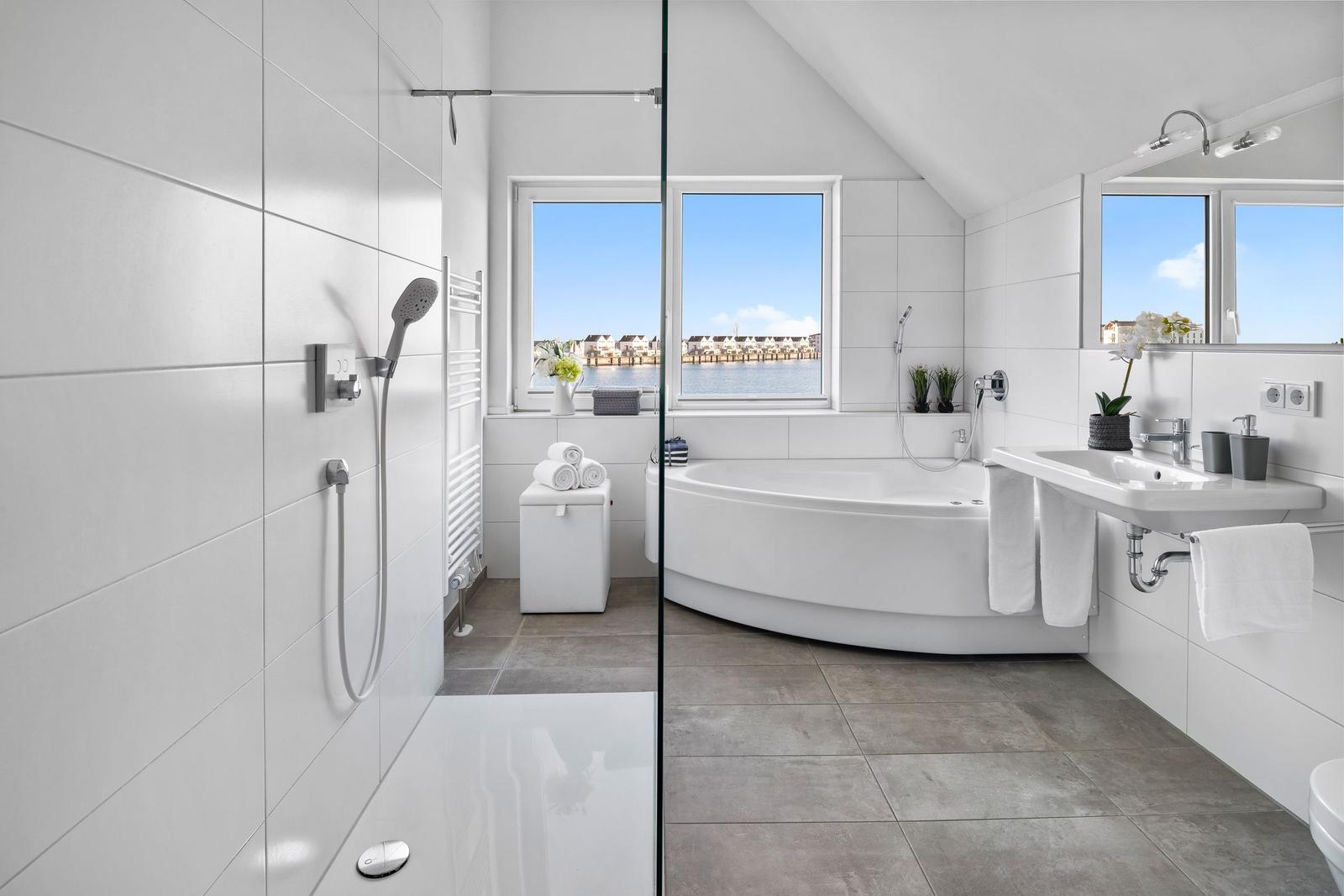 Badezimmer mit Dusche, Badewanne und Fensterblick auf Wasser.