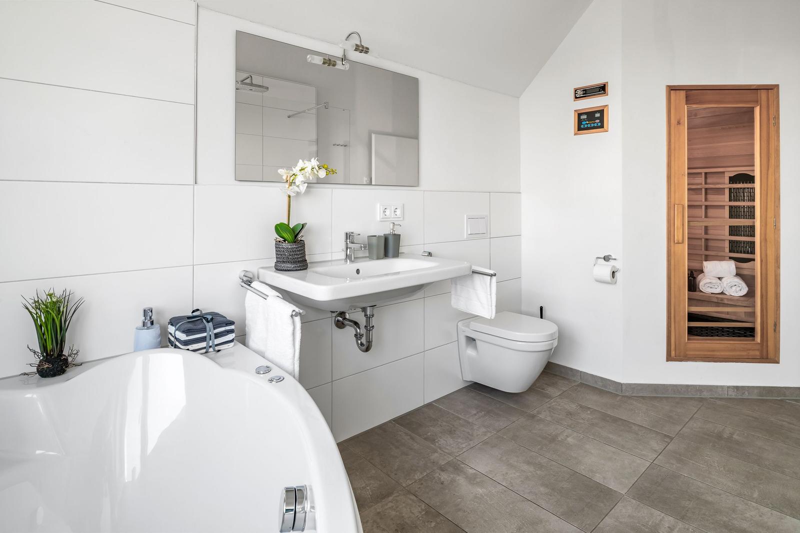 Bad mit Badewanne, Waschbecken und Sauna. Holztür und weiße Fliesen.