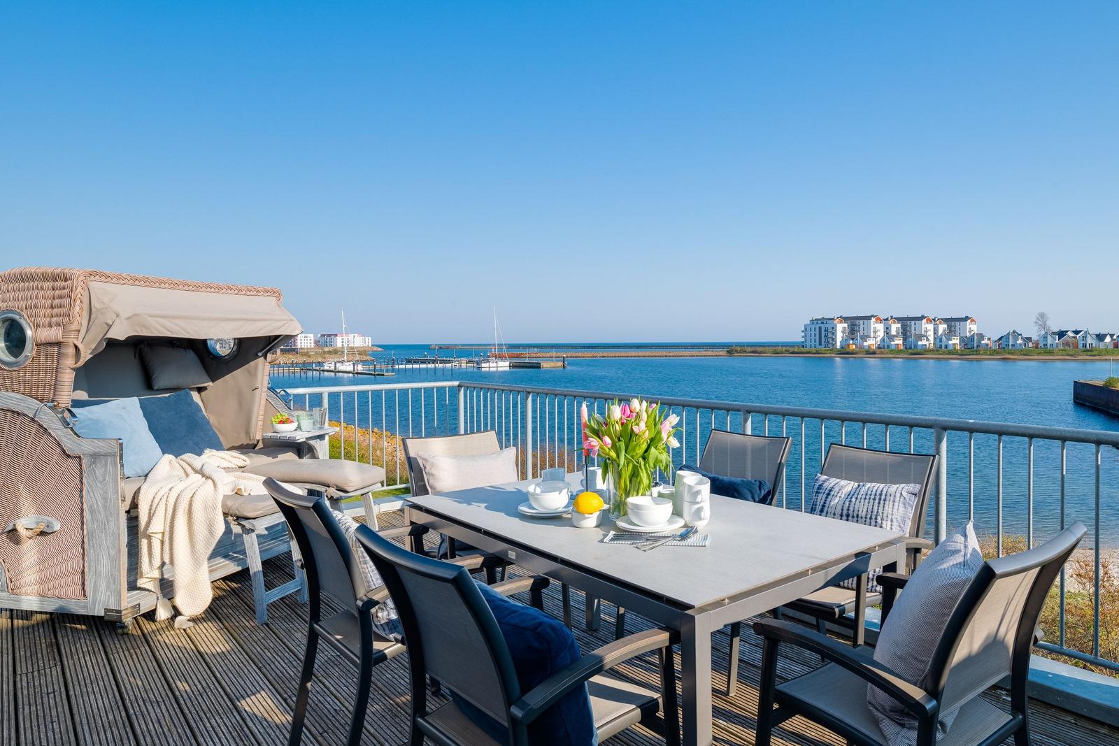 Terrasse mit Esstisch, Liegestuhl und Meerblick. Hintergrund: Wasser und Gebäude.