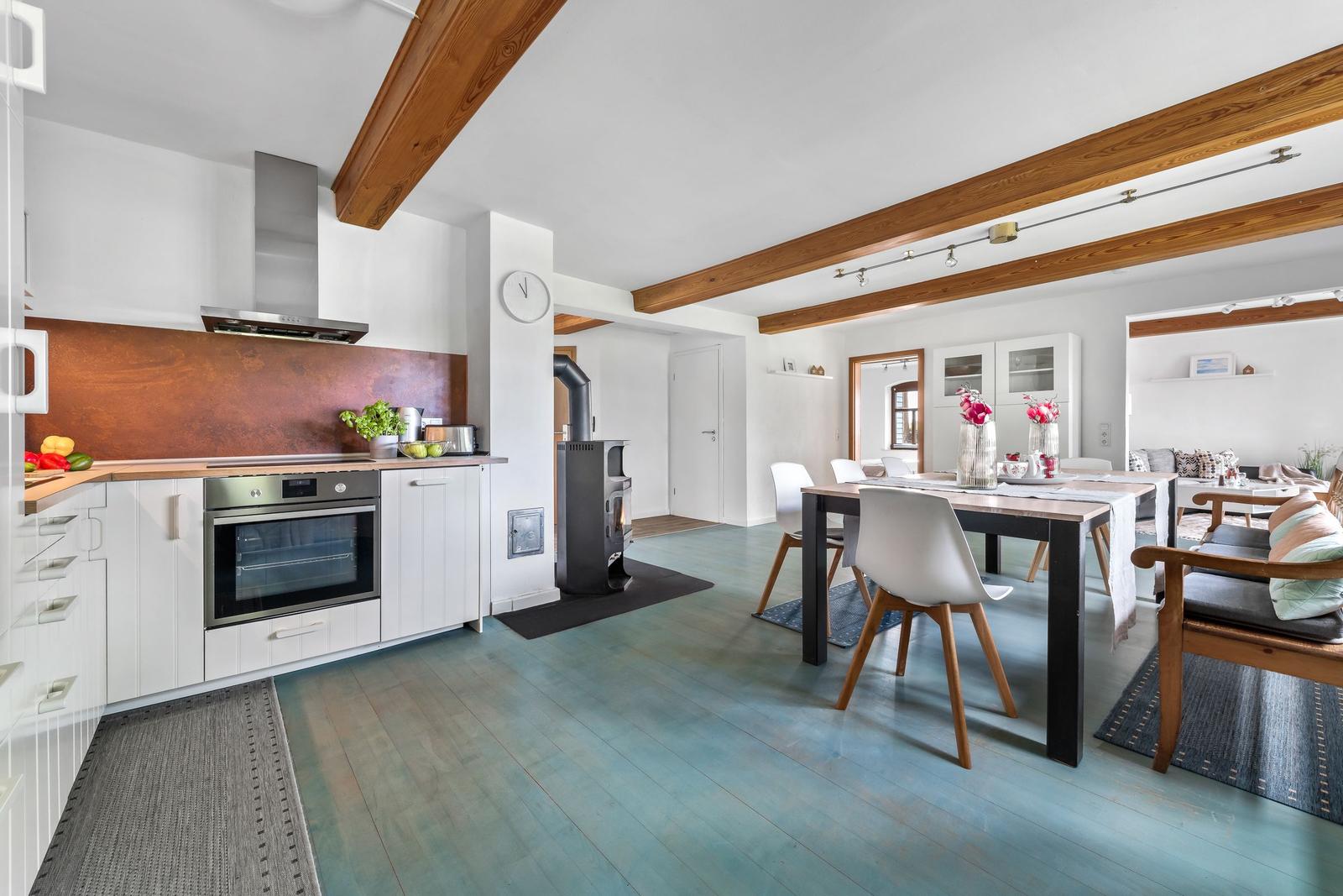 Küche mit Holzbalken, Esstisch und Wohnbereich mit Sofa und Stühlen.