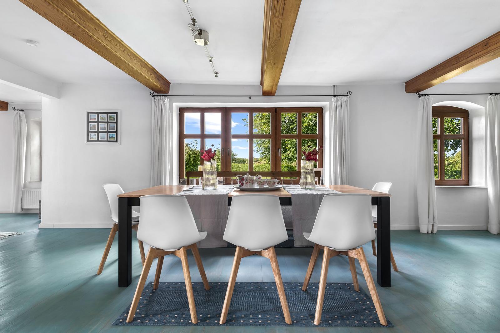 Esszimmer mit Holzdeckenbalken, Tisch mit Stühlen und Blick auf grüne Landschaft.