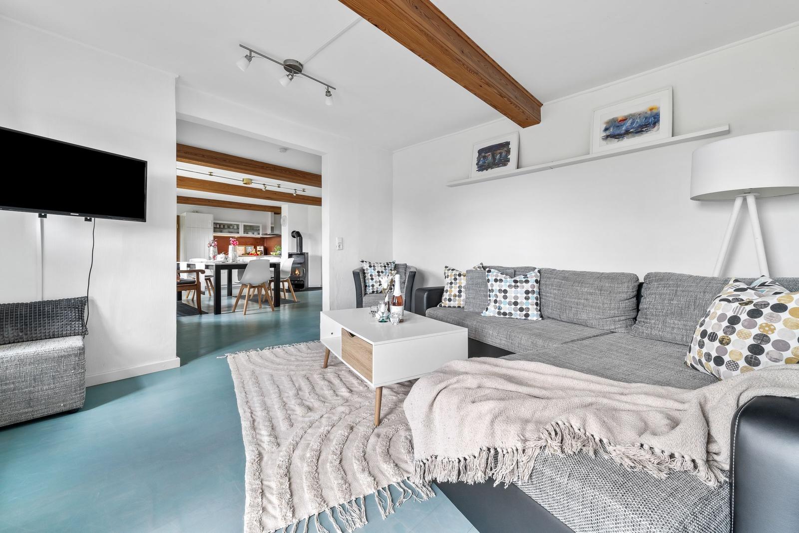 Wohnzimmer mit Sofa, Couchtisch und Fernseher. Durchgang zur Küche mit Esstisch.
