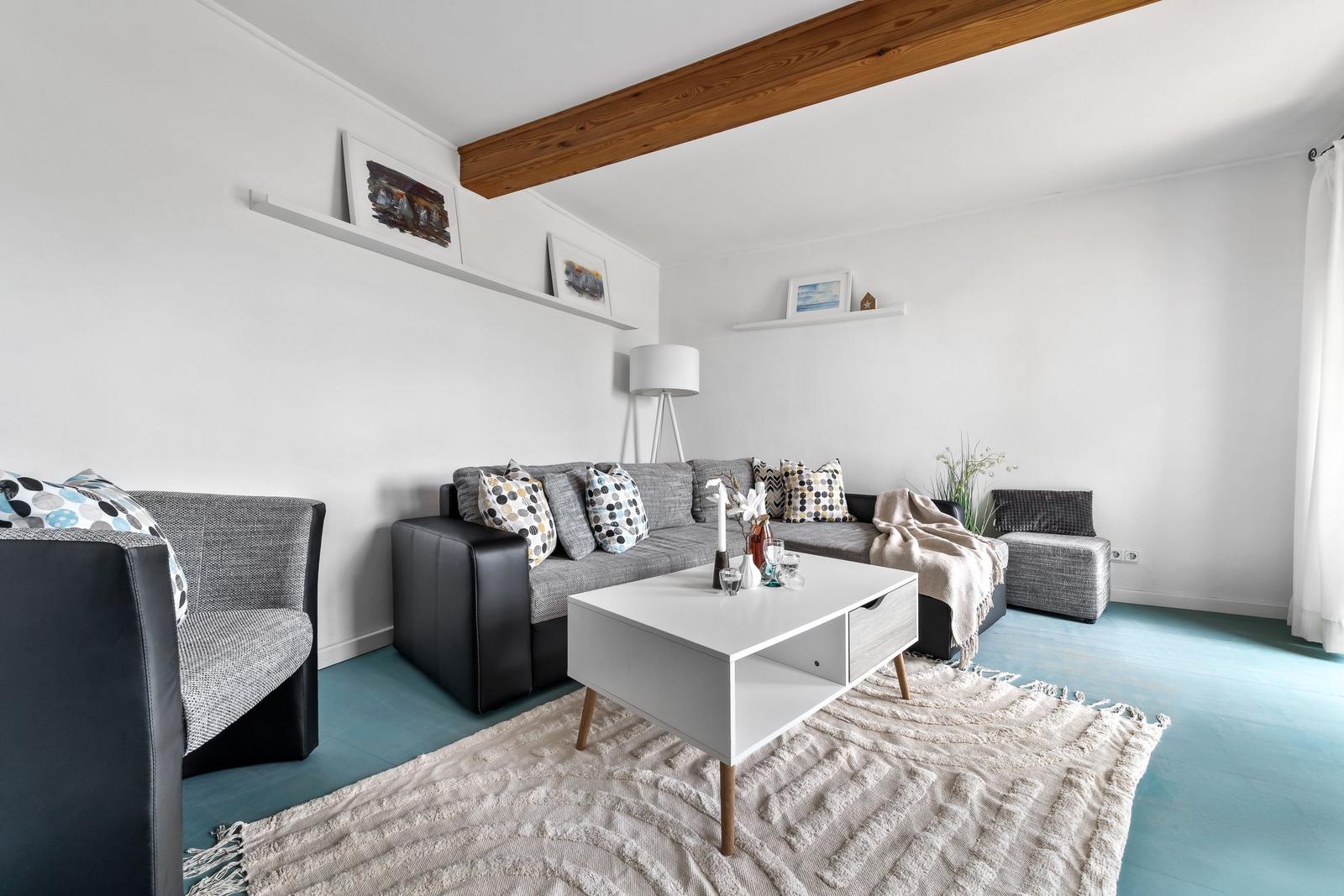 Wohnzimmer mit grauem Sofa, weißem Tisch und blauem Boden.