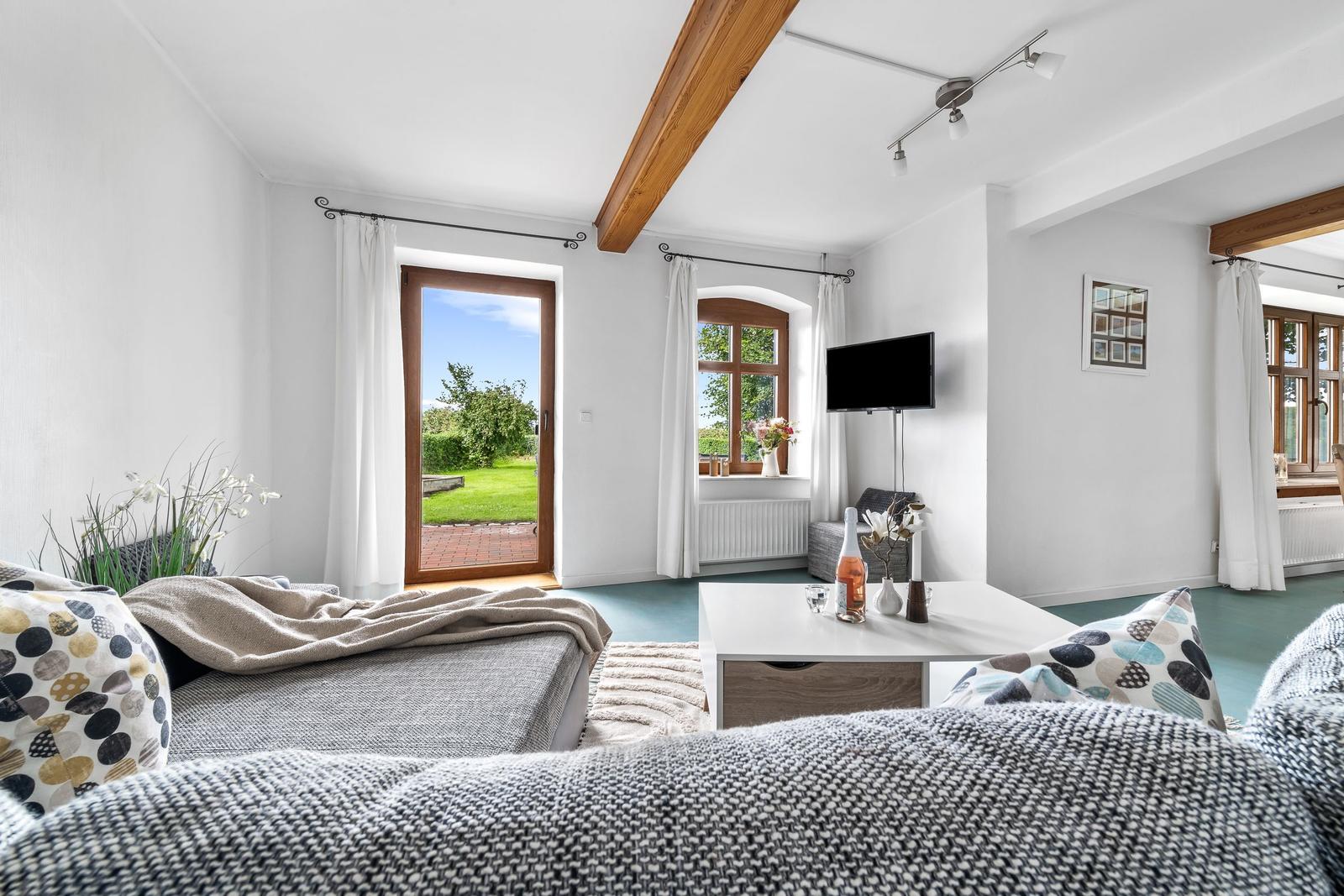 Wohnzimmer mit Sofa, Couchtisch und Fernseher. Durchgang zur Terrasse mit Blick auf Garten.