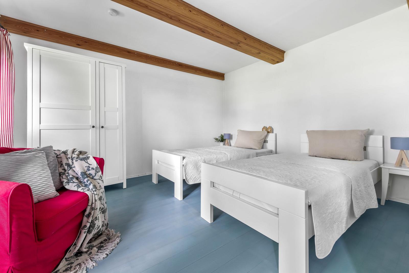 Zwei Betten, ein Sofa und ein Kleiderschrank in einem hellen Raum mit Holzbalken.
