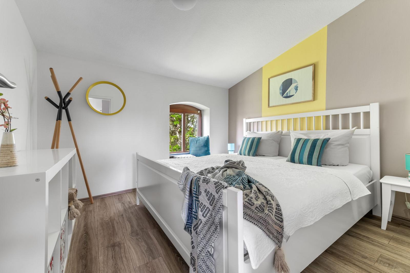 Schlafzimmer mit weißem Bett, Holzboden und gelbem Wandabschnitt.