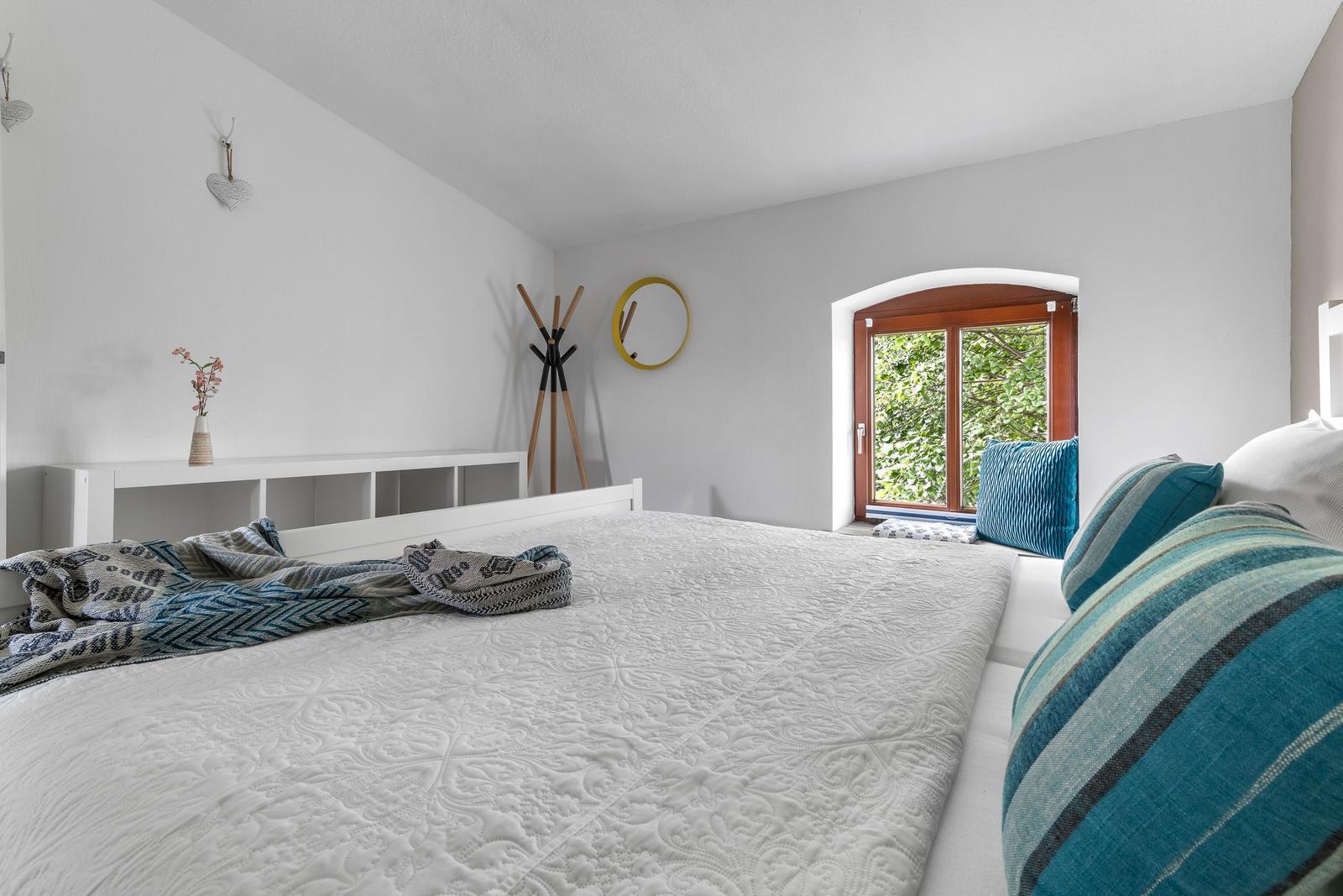 Schlafzimmer mit weißem Bett, blauen Kissen und Holztür zum Garten.